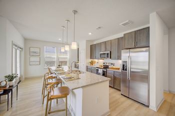 A modern kitchen with stainless steel appliances and wooden chairs.